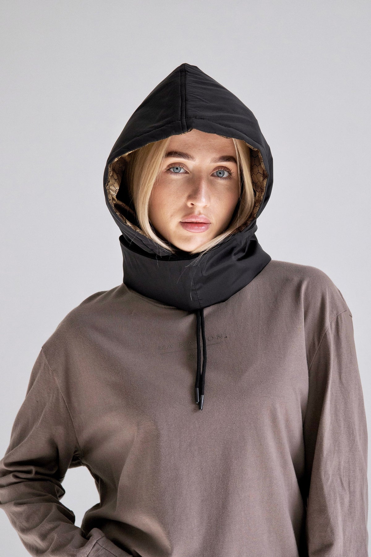 Person wearing a brown hoodie with a black hood against a plain background